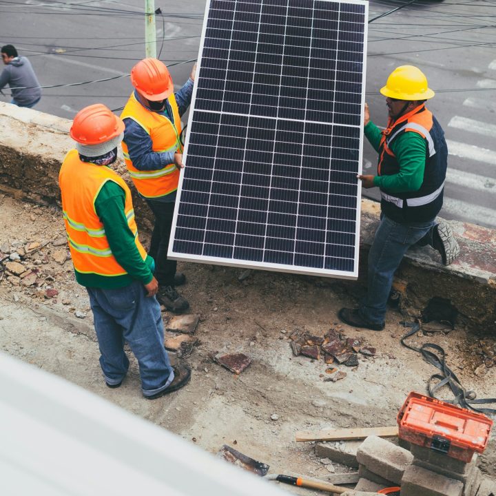 Workers in safety gear installing a solar panel outdoors.